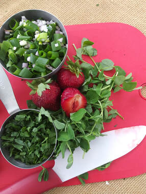 Strawberries and herbs being prepped on a cutting board